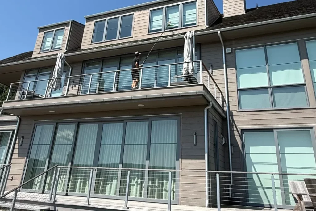 MJK Solutions technician cleaning the upper windows and glass railings of a contemporary home in the Hudson Valley