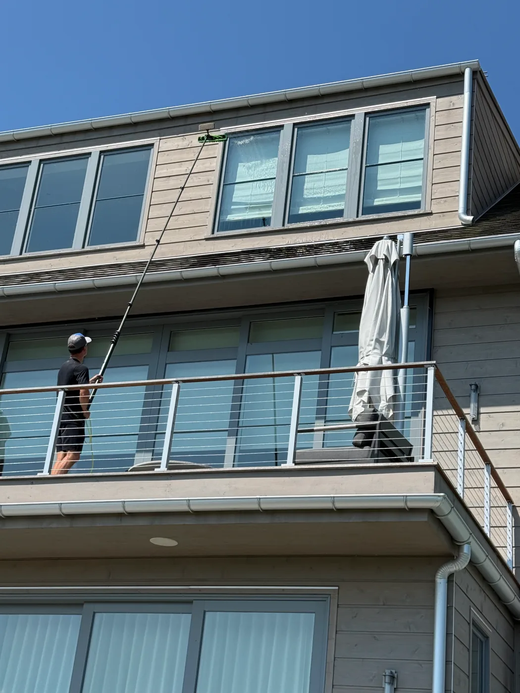 MJK Solutions technician cleaning upper-story exterior windows with a water-fed pole at a contemporary Hudson Valley home