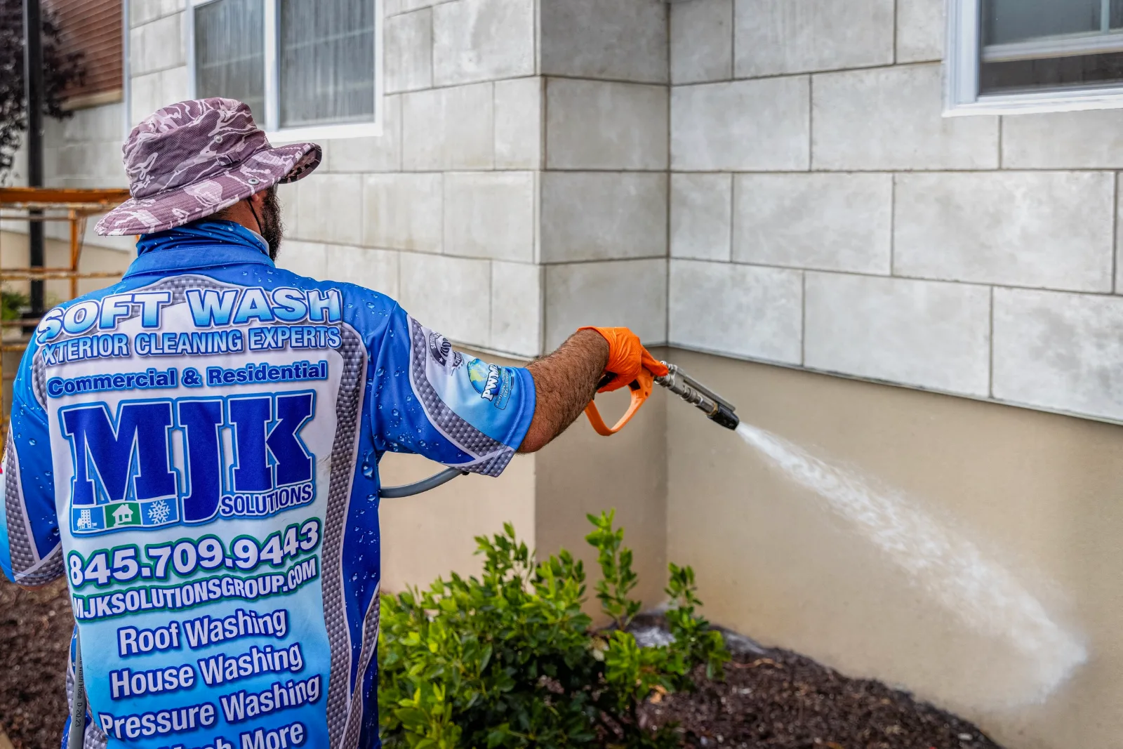 MJK Solutions technician in a branded shirt soft washing stucco siding at a Hudson Valley home