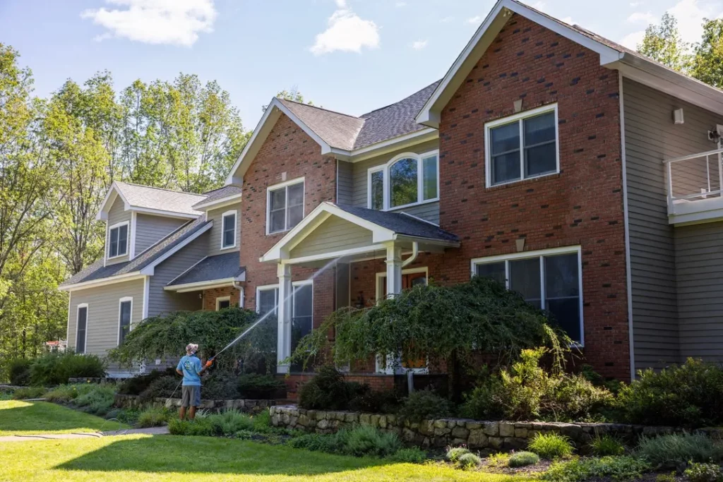 MJK Solutions technician soft washing a brick and vinyl colonial home in Dutchess County, NY