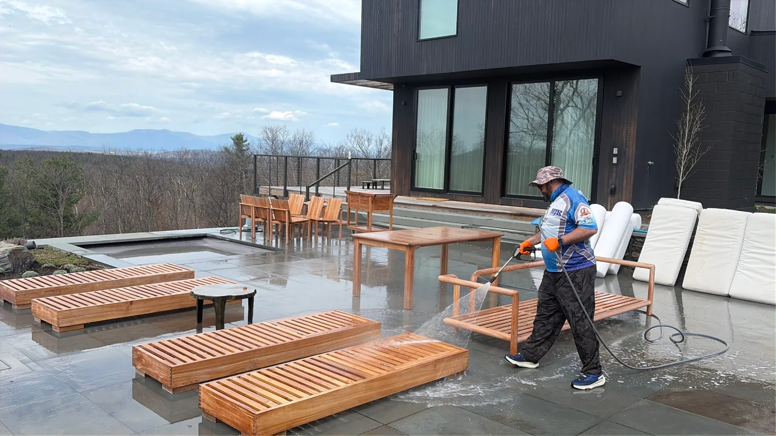 MJK Solutions technician pressure washing a stone patio and pool deck at a modern home overlooking the Hudson Valley