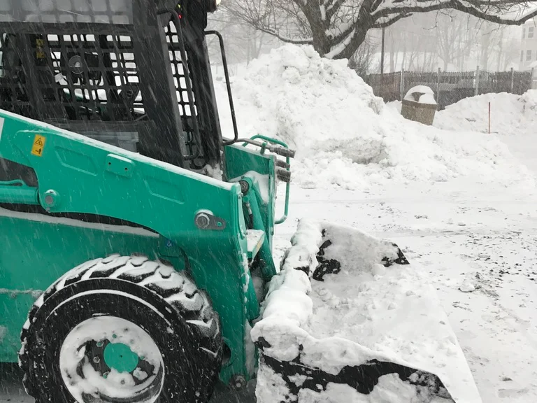Skid steer moving snow at a commercial property during snow removal by MJK Solutions in Poughkeepsie, NY