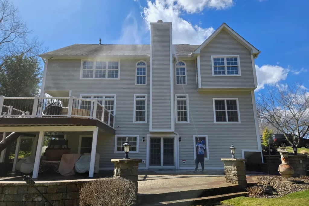 Rear of a large vinyl-sided colonial with a deck and stone patio being soft washed by MJK Solutions, Hudson Valley NY
