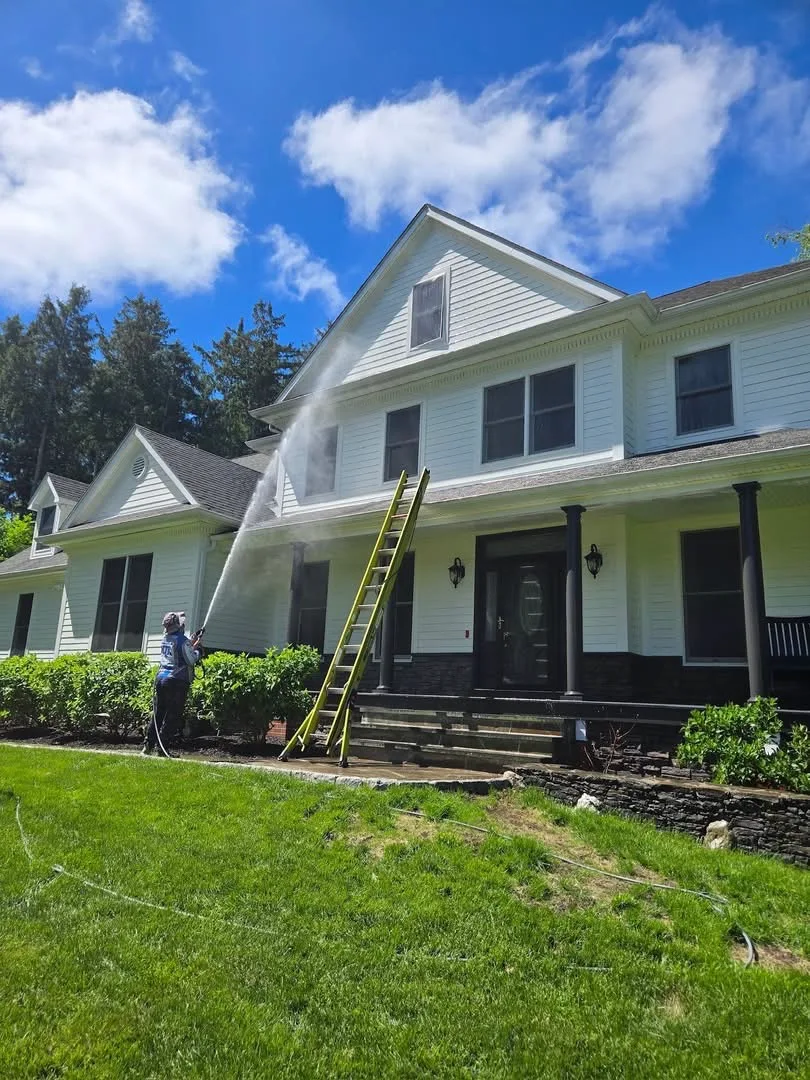 MJK Solutions technician soft washing the siding of a white farmhouse in Dutchess County, NY