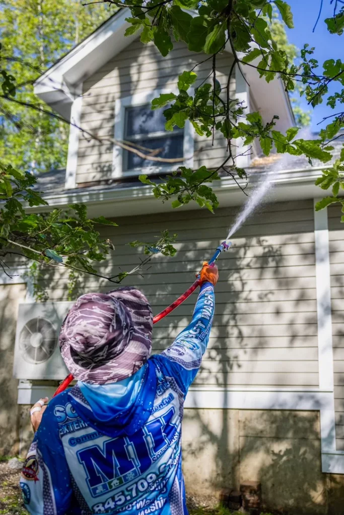 MJK Solutions technician soft washing green algae from the shaded siding of a Dutchess County home