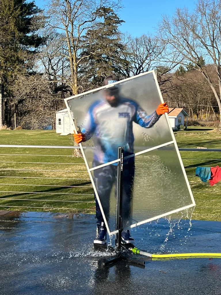 MJK Solutions technician washing a window screen on a screen-cleaning stand in Poughkeepsie, NY
